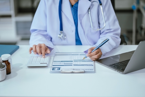 pic of medical person cant see face writing on a paper that looks like a bill and has a calculator