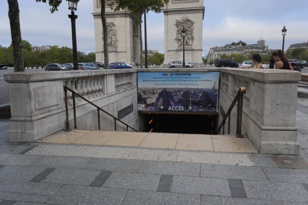 Steps leading down to the entrance of the Arc de Triomphe in Paris, featuring a bilingual sign promoting the view from the terrace.