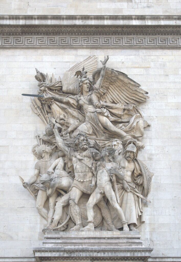 A detailed sculptural relief depicting a winged figure of victory leading a group of historical warriors, showcasing strength and bravery, set against a stone backdrop.