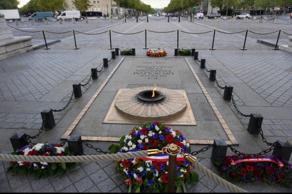 A view of the Eternal Flame surrounded by floral tributes, symbolizing remembrance and honor at a memorial site.