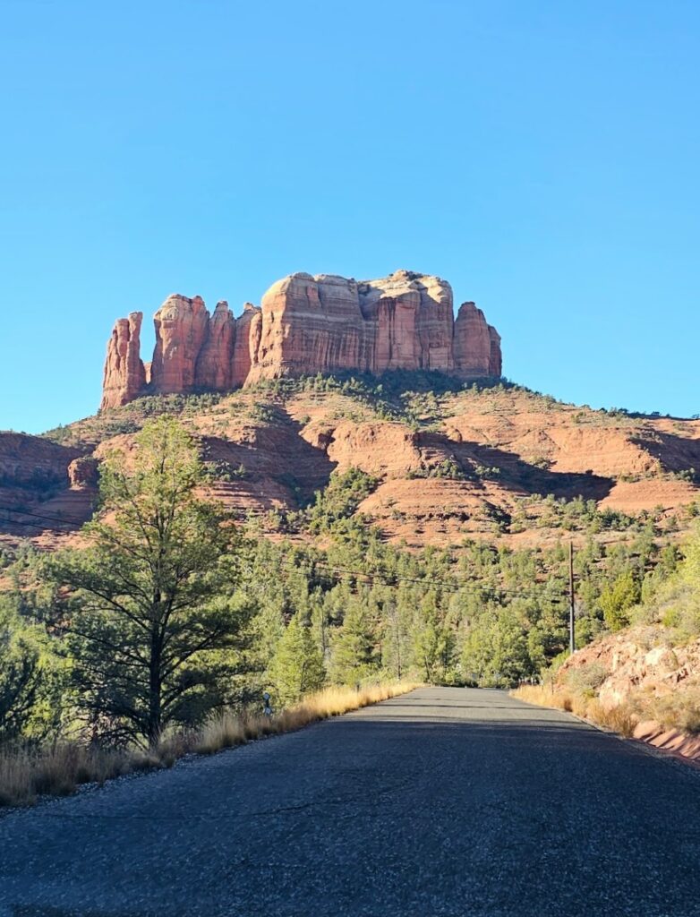 A scenic view of a winding road leading to majestic red rock formations under a clear blue sky.