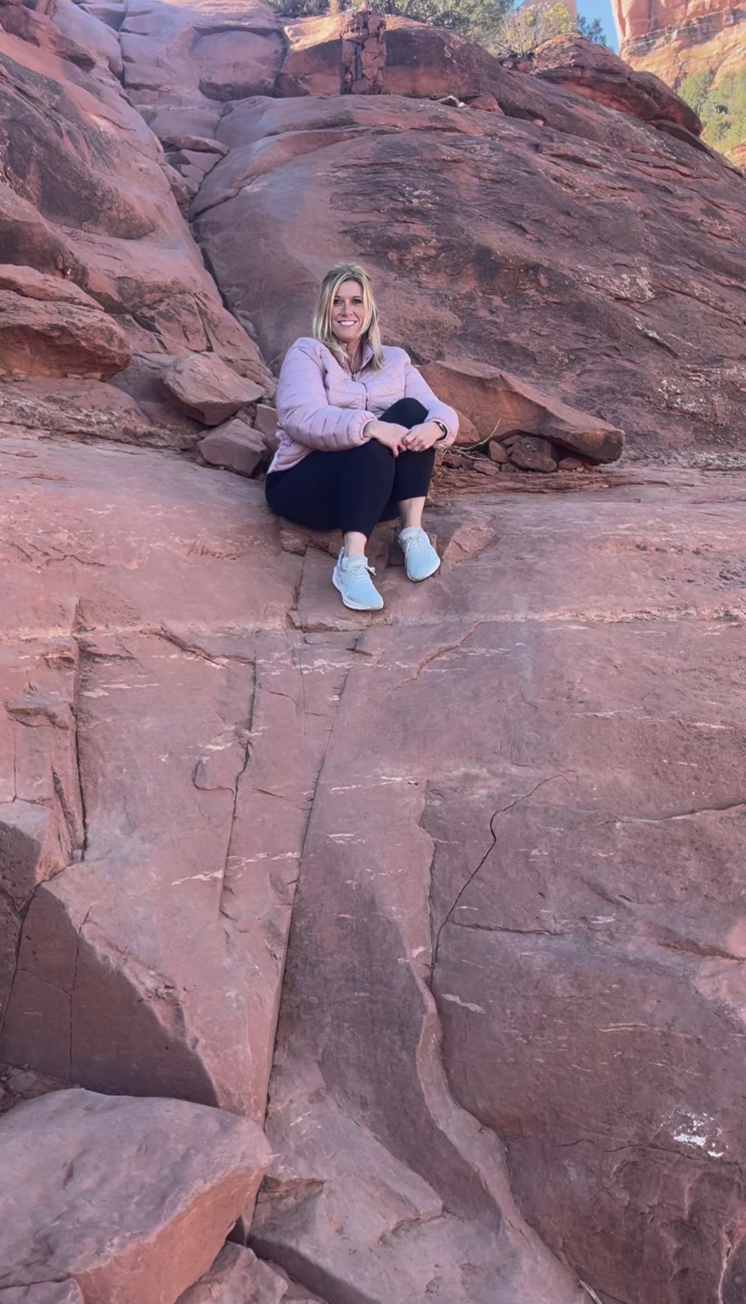 A woman sits on a rock formation, smiling and enjoying the scenery in a natural outdoor setting.