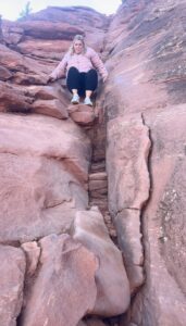 Person cautiously navigating a rocky slope while seated, with steep, natural rock formations in the background.