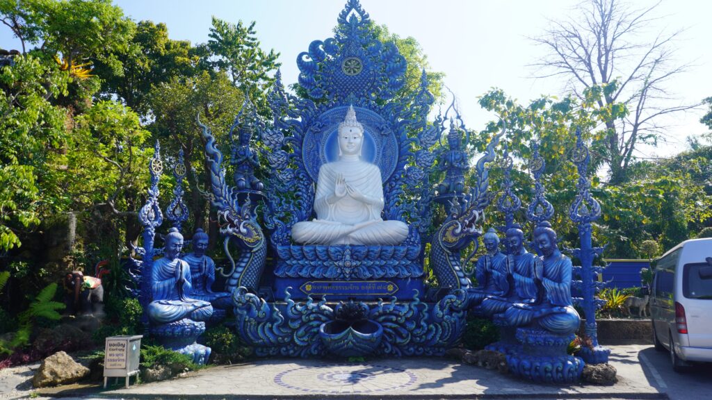 A stunning blue Buddhist statue accompanied by intricate blue figures and lush greenery in a serene outdoor setting.