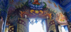 A beautifully detailed mural depicting Buddhist themes, intricate designs, and ornate doorways inside a temple, with natural light illuminating the scene.