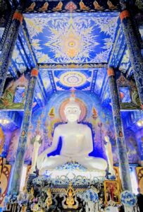 The White Temple, Chiang Rai A serene white Buddha seated in a colorful temple adorned with intricate blue and gold murals and decorative pillars.