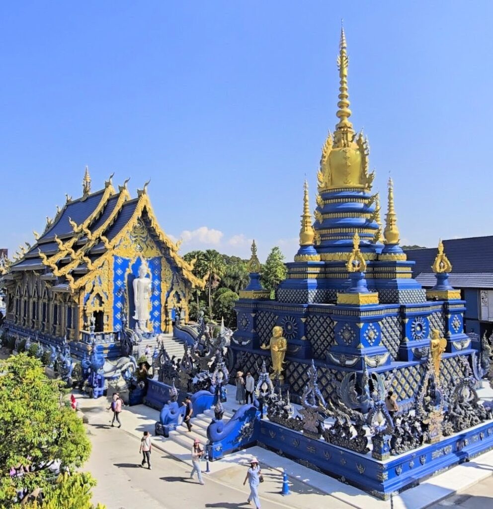 A panoramic view of the stunning Blue Temple, featuring intricate blue and gold architecture alongside visitors exploring the site.
