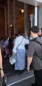 The White Temple, Chiang Rai A group of people entering a beautifully decorated building, with ornate columns and artistic wall designs, as they carry bags and engage in conversation.