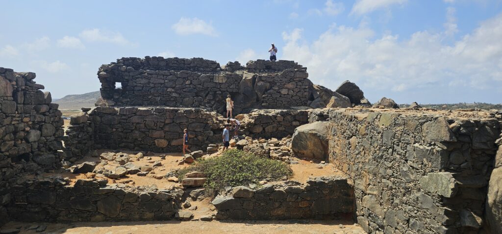 Visitors exploring stone ruins under a bright blue sky, surrounded by rocky terrain and greenery.