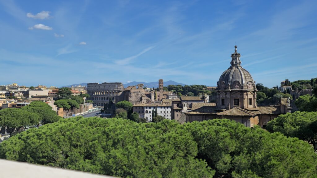 A stunning landscape showcasing iconic Roman architecture, including the Colosseum and historic buildings, surrounded by lush greenery under a bright blue sky.