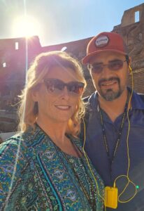 A couple takes a selfie at the Colosseum, with the sun shining brightly in the background.