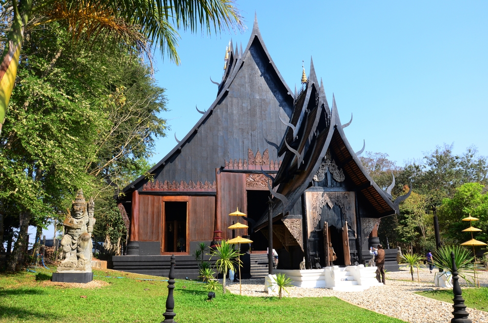 A beautifully designed traditional Thai building, showcasing intricate details and a unique roof style, surrounded by lush greenery and ornamental features.