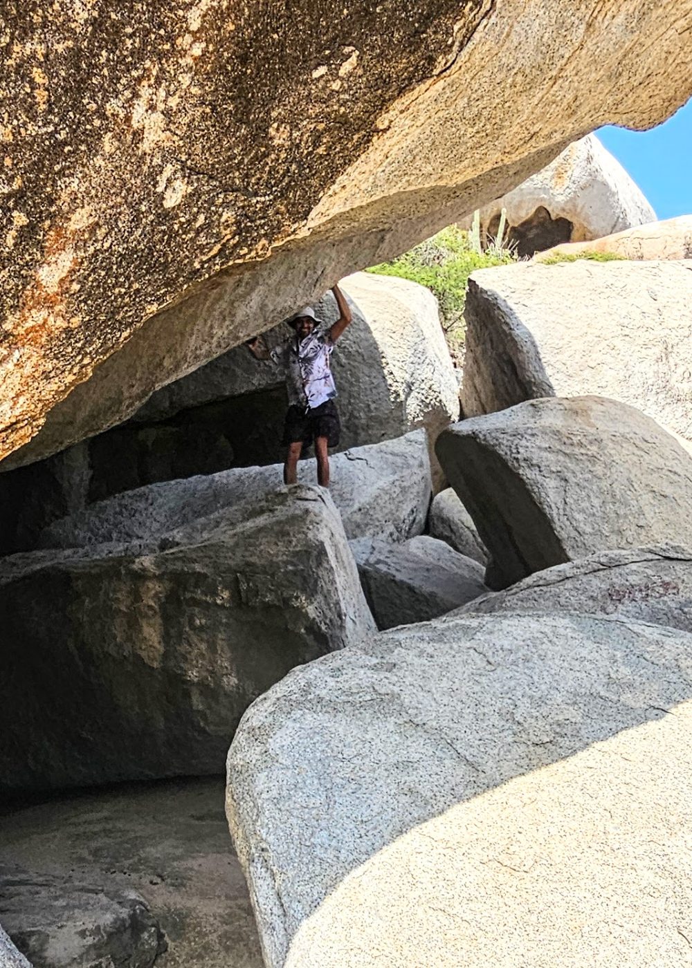 The Bushiribana Gold Mill Ruins In Aruba A person climbing and balancing on large boulders in a rocky landscape under a clear blue sky.
