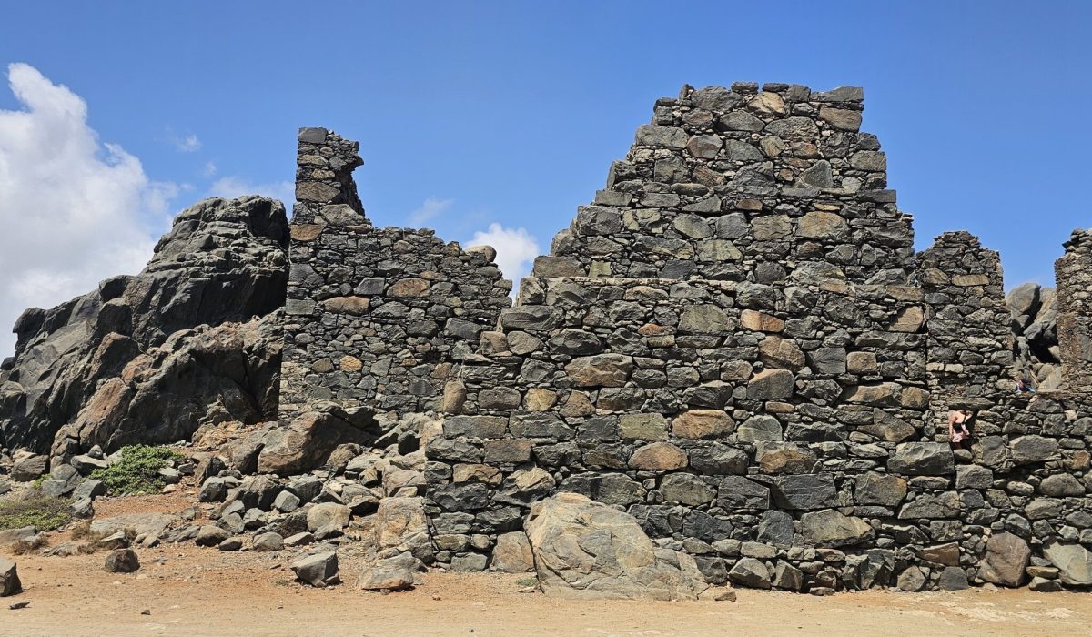 The Bushiribana Gold Mill Ruins In Aruba Weathered stone ruins against a clear blue sky, surrounded by rocky terrain and sparse vegetation.