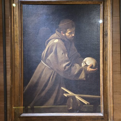 A monk holding a skull, deep in thought, framed by a wooden border.