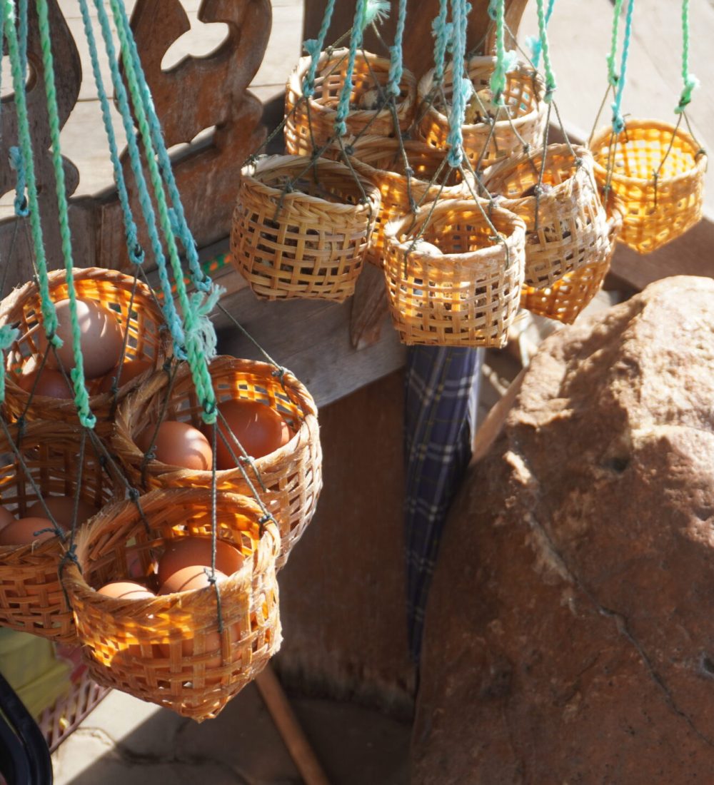 The White Temple, Chiang Rai A close-up view of several small woven baskets hanging with eggs, displayed against a rustic wooden background and a large rock.