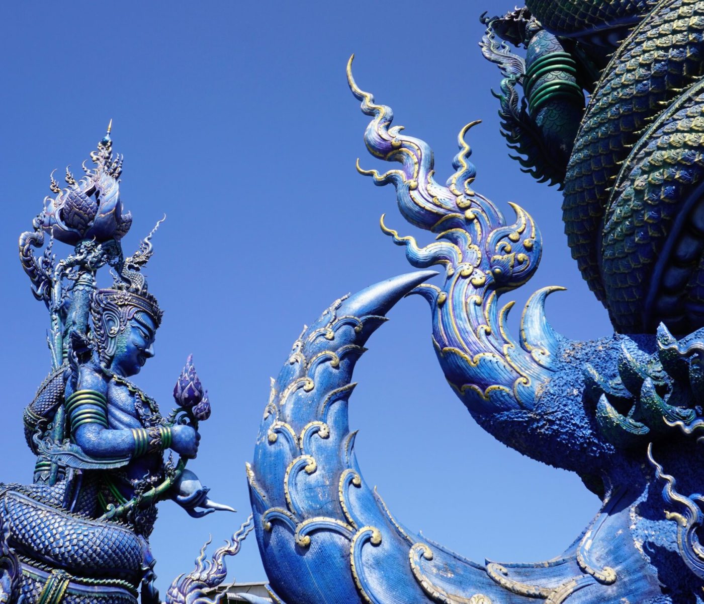 A detailed view of intricately designed blue statues against a clear sky, featuring a figure holding a lotus and a serpentine dragon-like creature.