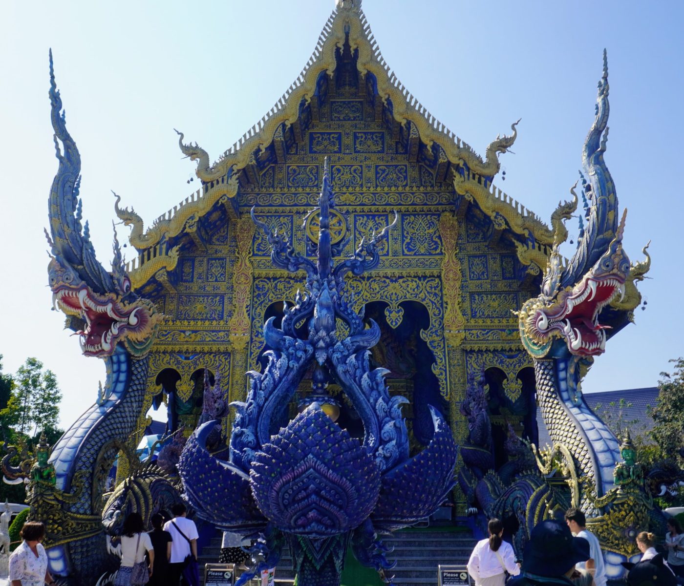 Stunning blue and gold facade of Wat Rong Suea Ten, featuring intricate dragon sculptures and visitors exploring the site.
