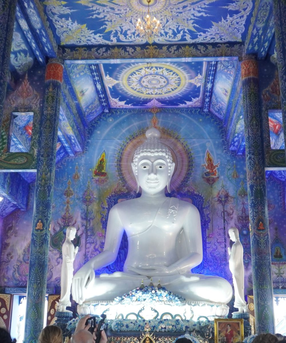 A peaceful view of the interior of a Buddhist temple featuring a large white Buddha statue surrounded by intricate blue murals and pillars.