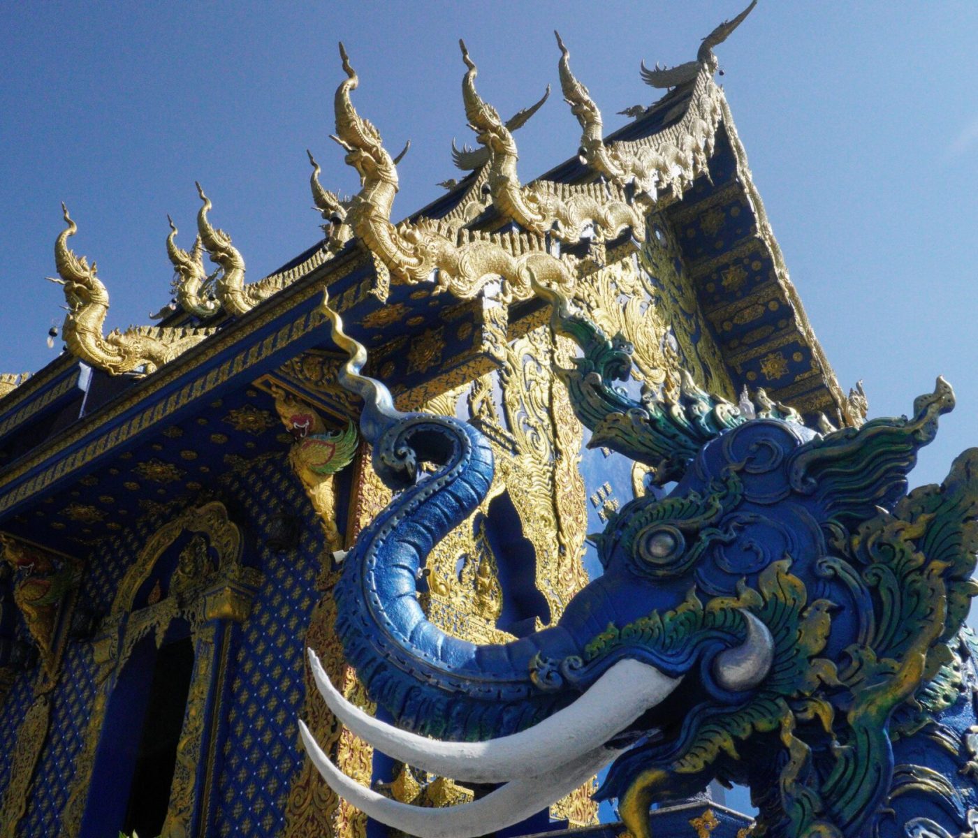 Close-up view of a richly decorated temple with intricate blue and gold details, featuring mythical creature sculptures against a clear blue sky.