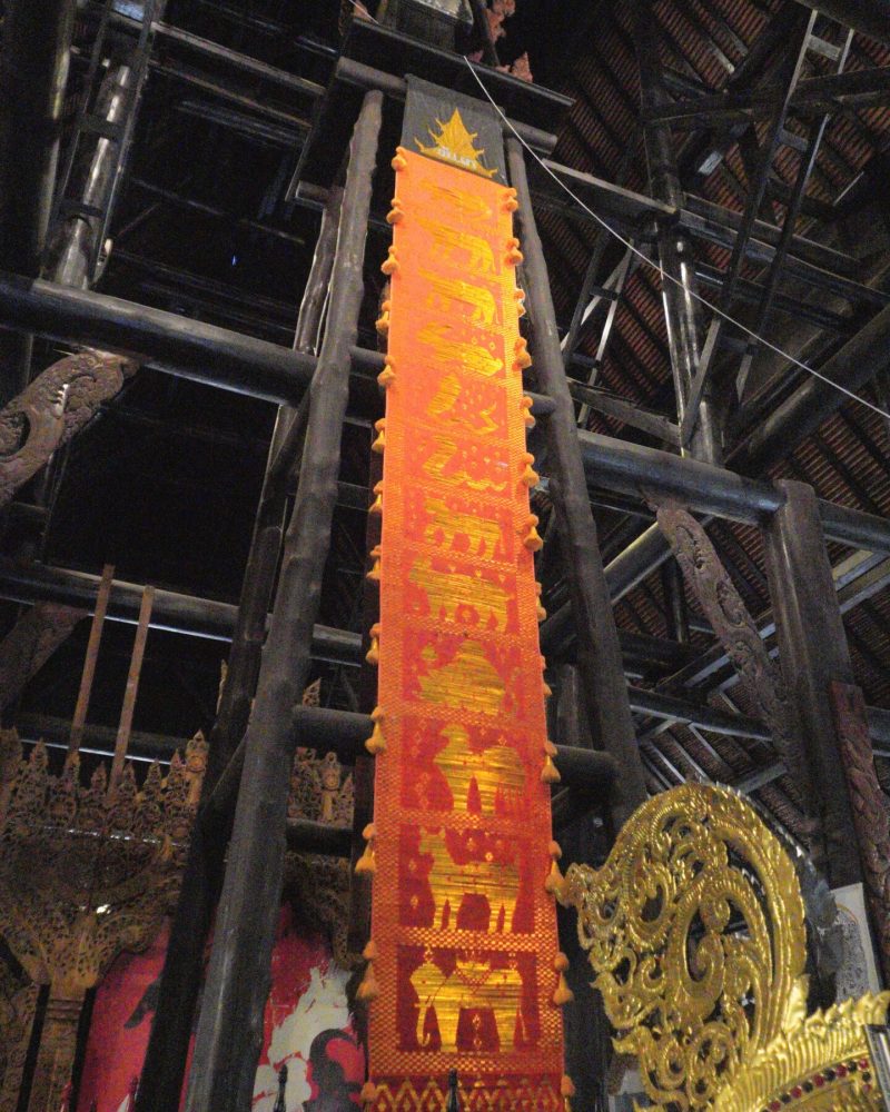 Baan Dam: The Black House Museum A view of an intricately decorated temple interior featuring an orange banner with golden designs and ornate golden sculptures in the foreground.