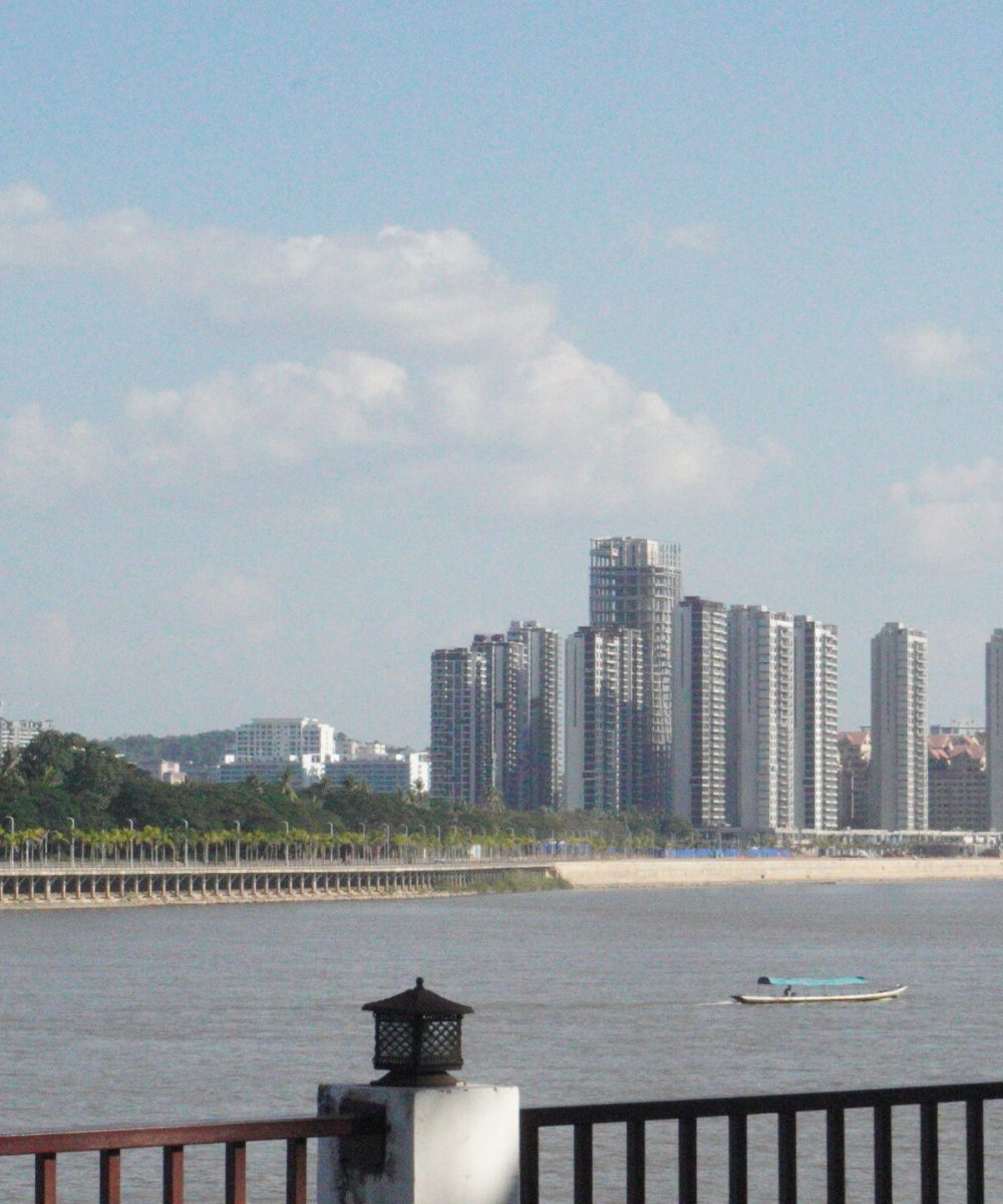 The White Temple, Chiang Rai A tranquil river view featuring modern buildings and a distinct, architectural structure under a clear blue sky.