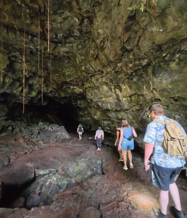 A group of hikers navigating through a rocky lava tube cave with an uneven ground and moss-covered walls.