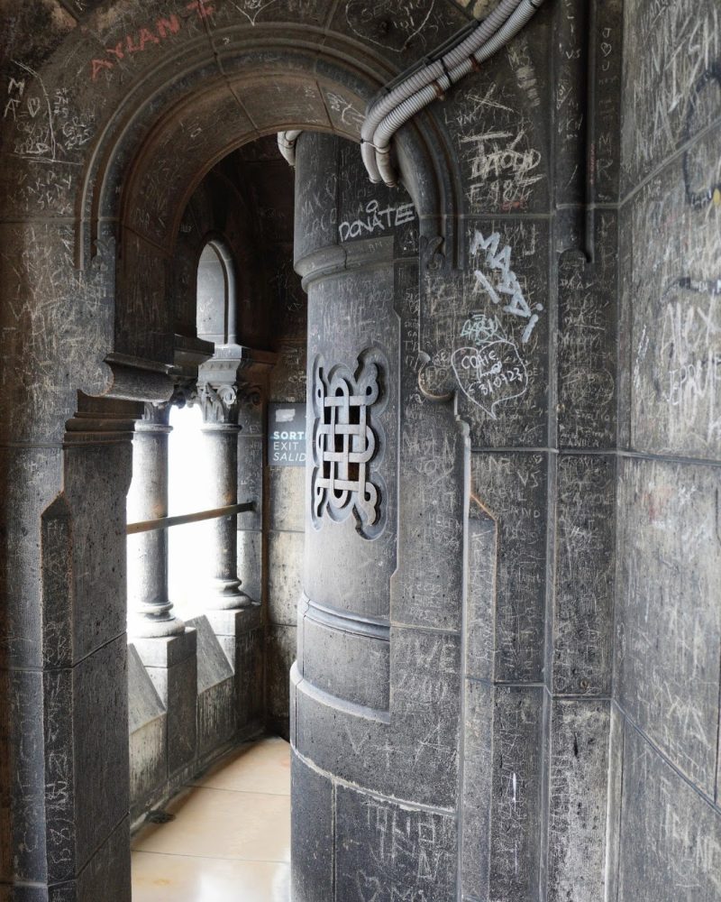 A stone archway featuring extensive graffiti on the walls, with a glimpse of natural light illuminating the interior space.