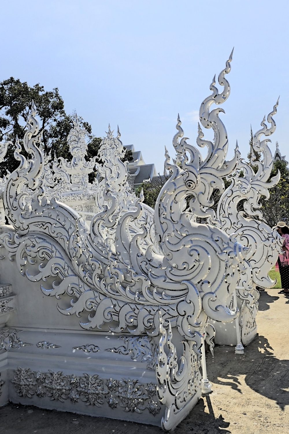 The White Temple, Chiang Rai Close-up of ornate white architectural elements with intricate designs and embellishments against a clear blue sky.