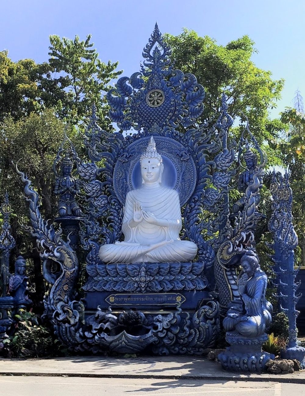 The White Temple, Chiang Rai A stunning blue Buddha statue surrounded by intricate designs and sculptures, set against a clear blue sky and lush greenery.