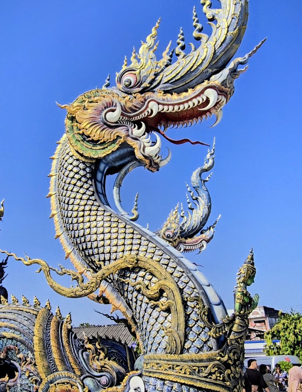 The White Temple, Chiang Rai Intricate dragon sculpture adorned with vibrant colors and ornate detailing, set against a clear blue sky.