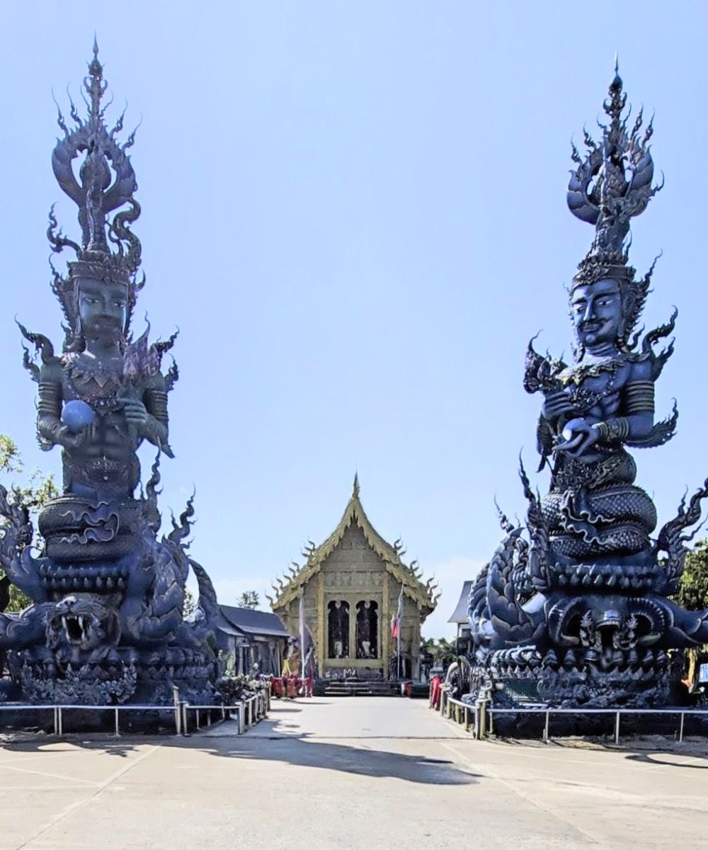 A stunning view of two large black statues flanking a golden temple, set against a clear blue sky.