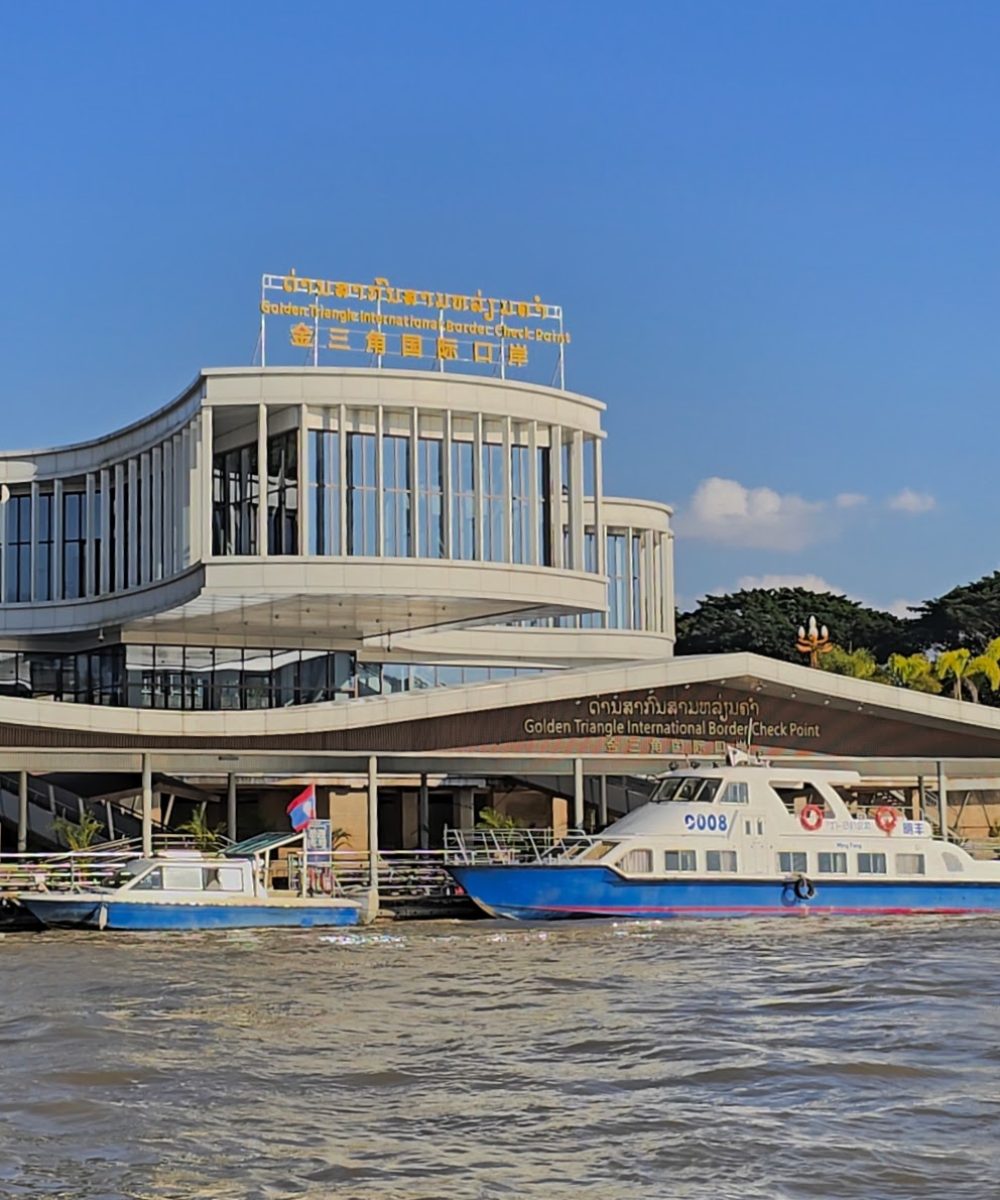 The White Temple, Chiang Rai View of the Golden Triangle International Border Check Point with boats docked at the riverside under a clear blue sky.