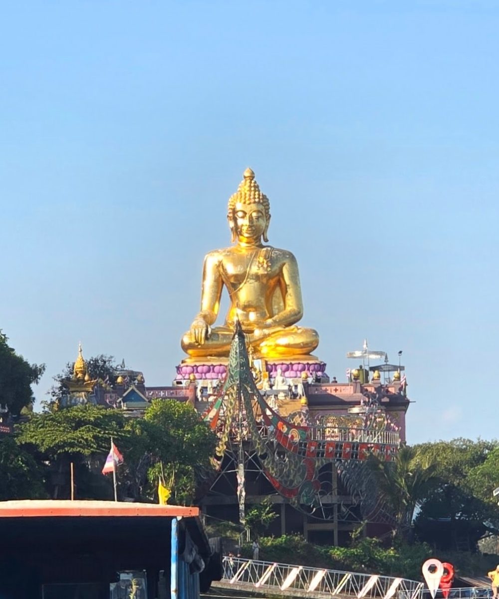 The White Temple, Chiang Rai A majestic golden Buddha statue sitting atop a temple, surrounded by lush greenery and clear blue skies.