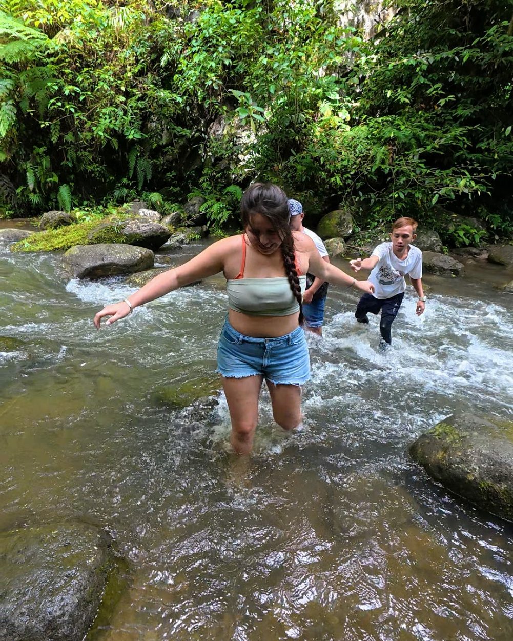 People wading through a stream in a lush, green environment, enjoying a day of exploration.