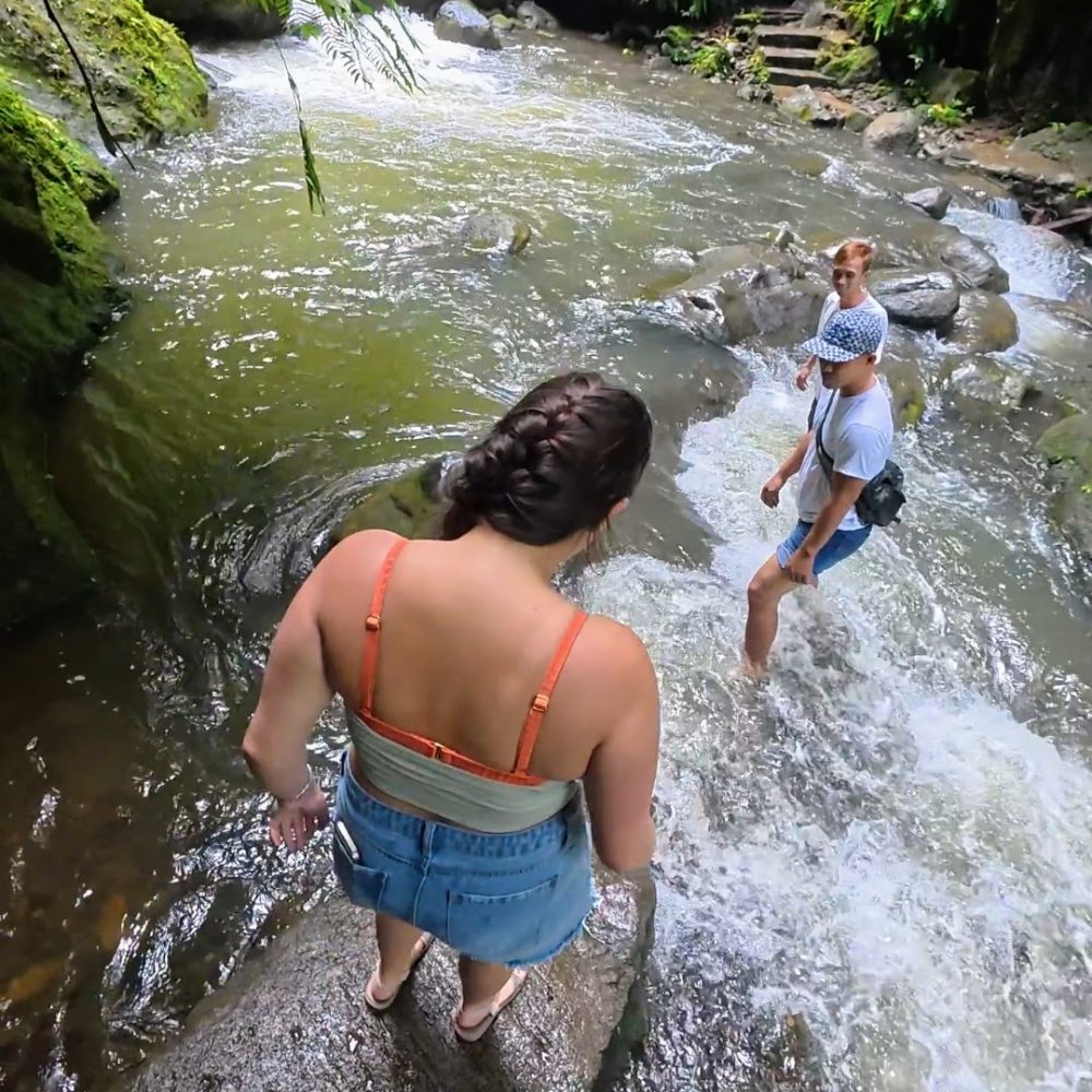Casaroro Falls — An Adventurous Hike That Was A Little More Than I Expected A group of friends navigating a rocky riverbank surrounded by lush greenery and flowing water.