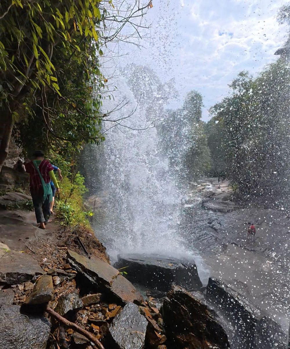 Overnight Stay At Chai Lai Orchid Elephant Sanctuary in Thailand A stunning view of a waterfall with mist and splashes captured as people walk along a rocky path.