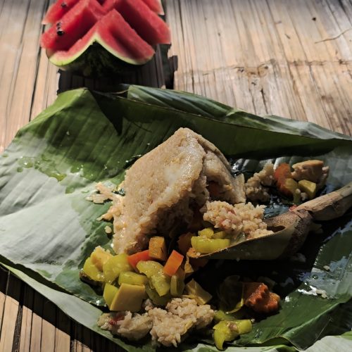 Overnight Stay At Chai Lai Orchid Elephant Sanctuary in Thailand A serving of traditional dish on a banana leaf with colorful vegetables, accompanied by slices of watermelon in the background.