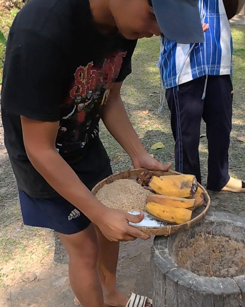 Overnight Stay At Chai Lai Orchid Elephant Sanctuary in Thailand A person holding a basket of bananas and grain, preparing for cooking outdoors.