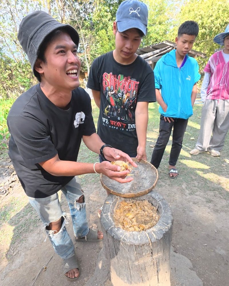 Overnight Stay At Chai Lai Orchid Elephant Sanctuary in Thailand Young men engage in traditional processing of natural materials, showcasing collaboration and local practices in a vibrant outdoor environment.
