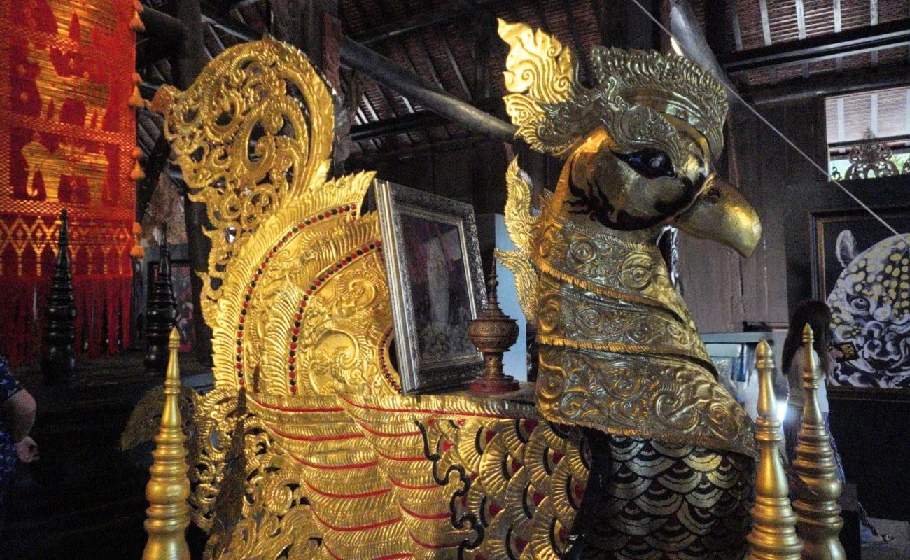 Baan Dam: The Black House Museum Intricately designed golden sculpture of a mythical bird adorned with red accents, set against a backdrop of ornate wall decorations and artwork.