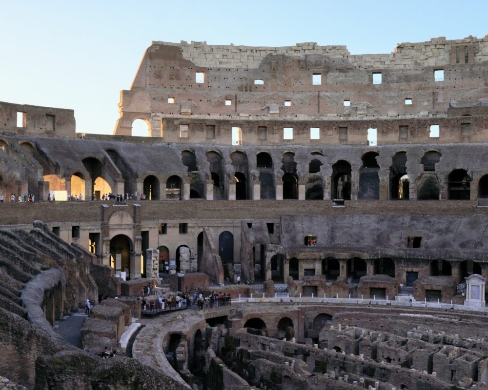A panoramic view of the interior of the Roman Colosseum showcasing its arches, stone layout, and visitors exploring the ancient structure.