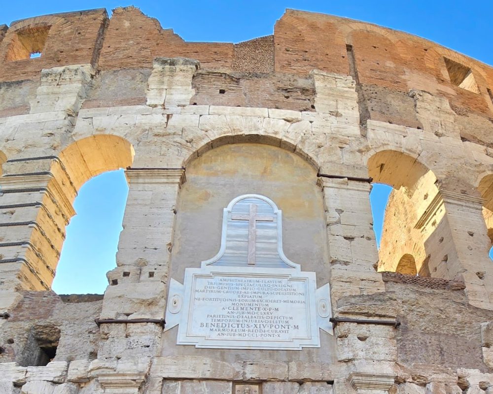 A close-up view of an archway in the Roman Colosseum, featuring historical carvings and a clear blue sky in the background.