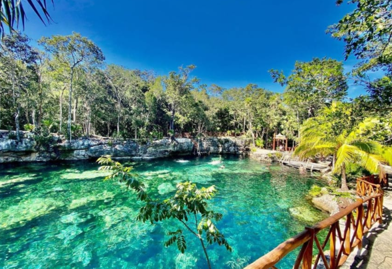 Crystal-clear cenote surrounded by lush jungle and wooden railings in Riviera Maya, Mexico