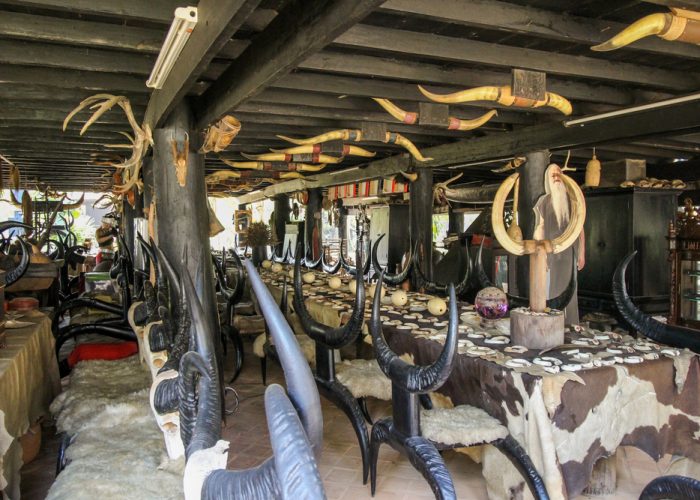Baan Dam: The Black House Museum An interior view of a rustic dining room featuring dark wooden beams, tables adorned with horn decorations, and various artifacts, creating a unique and eclectic atmosphere.